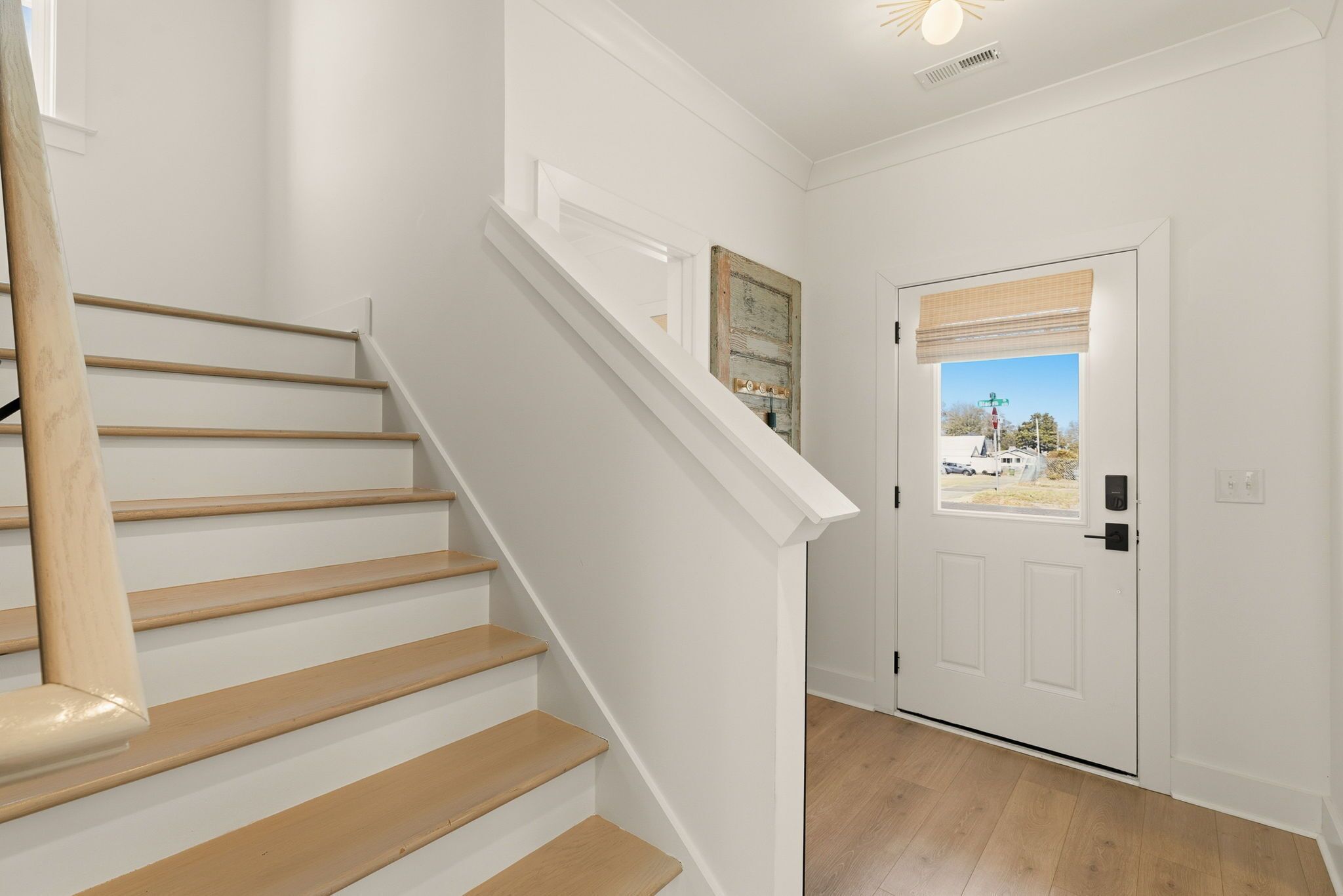 A staircase with wooden steps and white walls, leading to a door with a view of the outside.