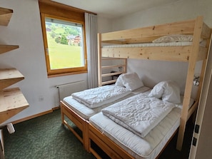 A bunk bed room with a window, a radiator, and a green carpet.