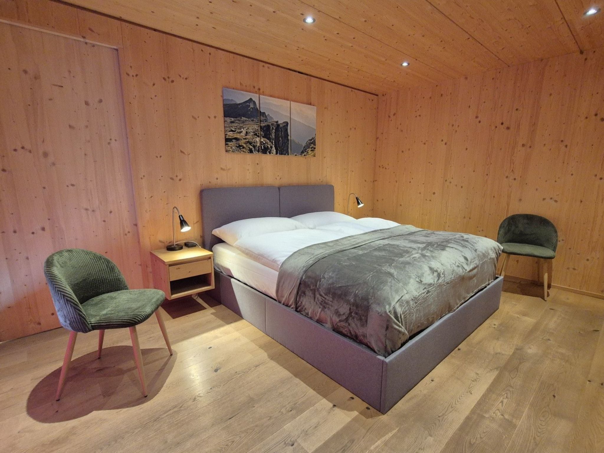 A bedroom with a bed, a nightstand, a chair, and a wooden wall.