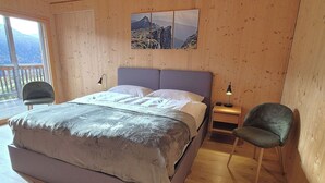 Een kamer met houten lambrisering, een bed, een stoel, een nachtkastje en een raam met uitzicht op bergen.