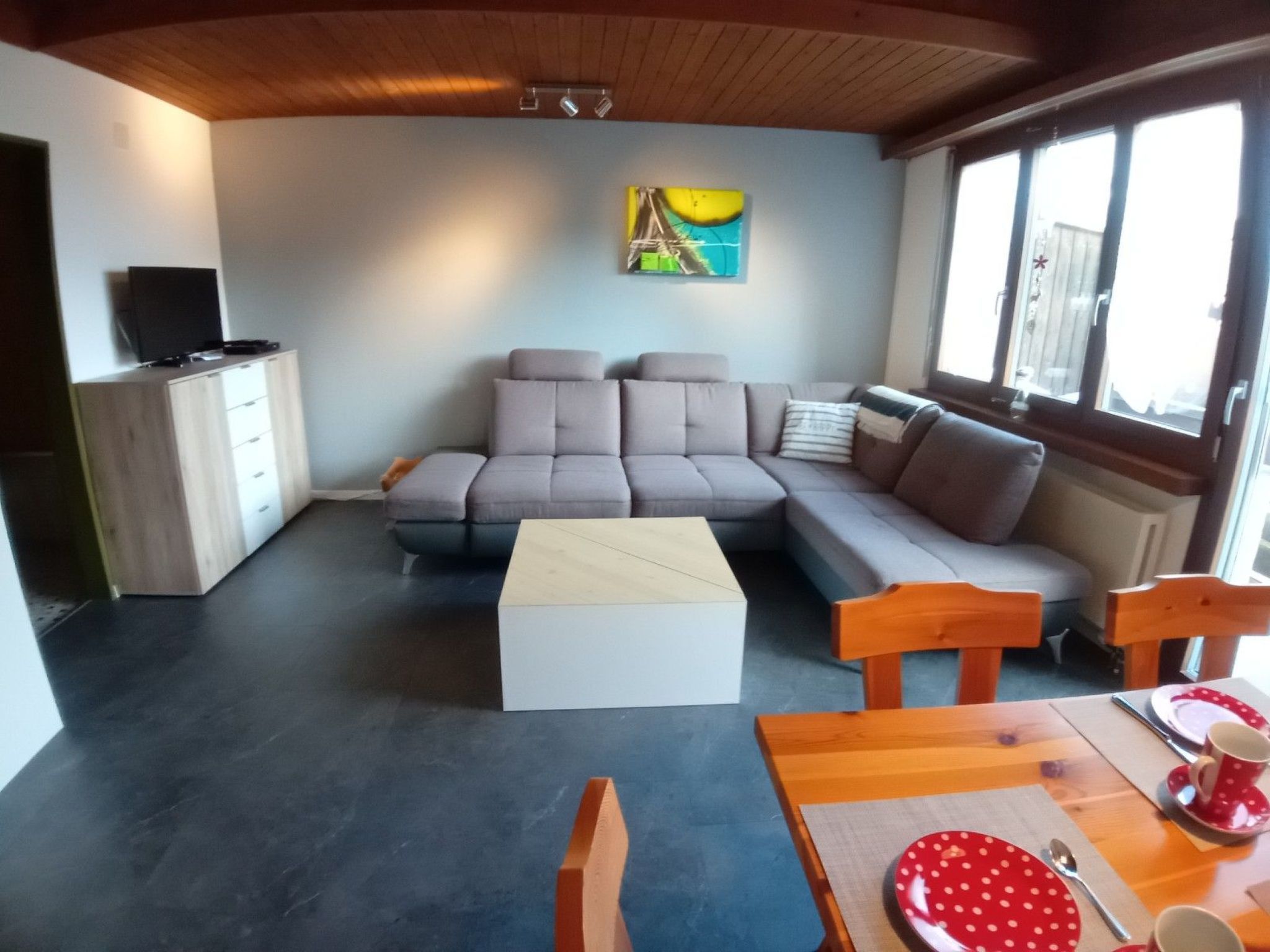 Een woonkamer met een modulaire bank, een salontafel, een eettafel met stoelen en een schilderij aan de muur.