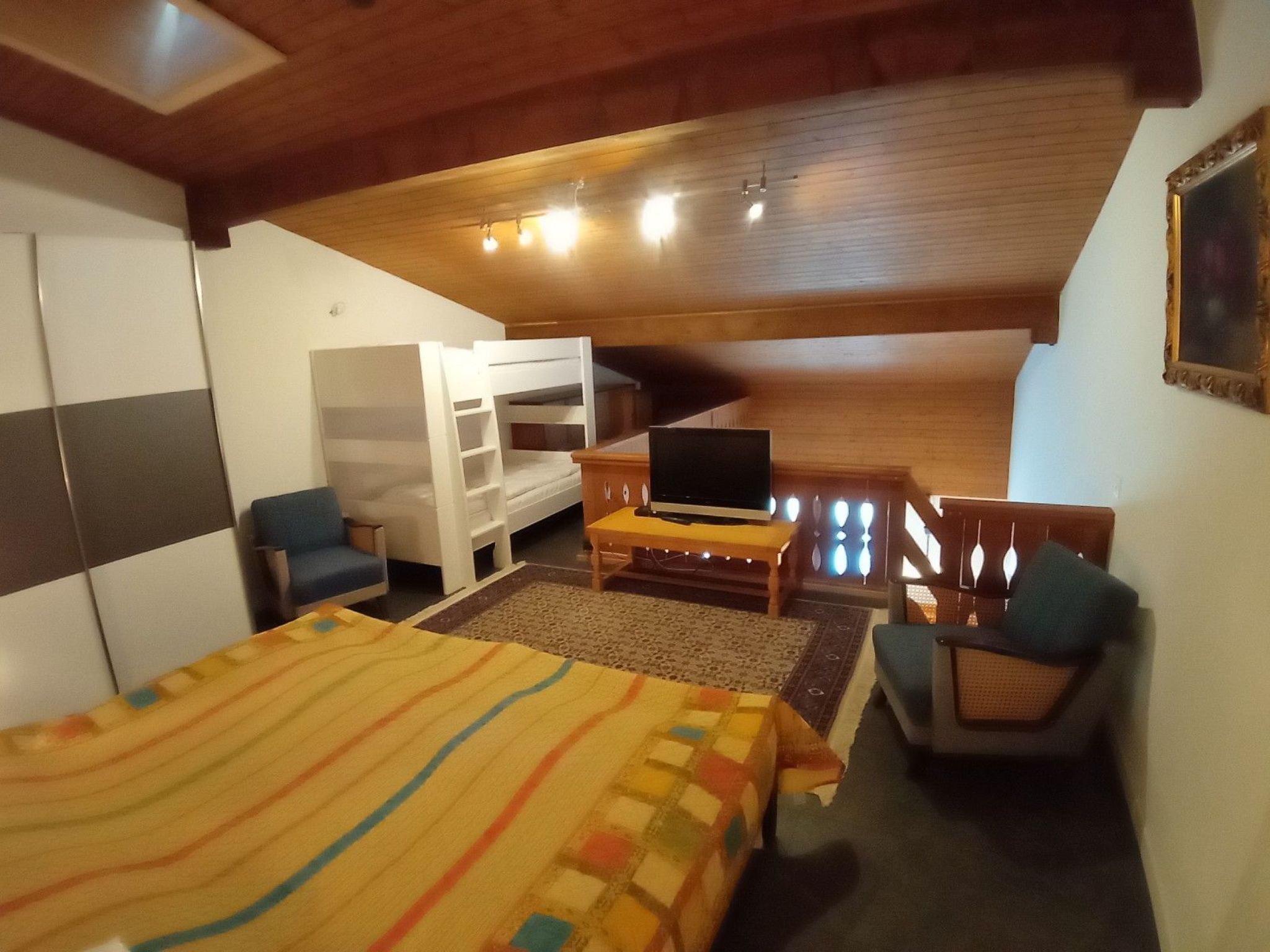 A room with a bunk bed, a desk with a television, a chair, and a wardrobe.