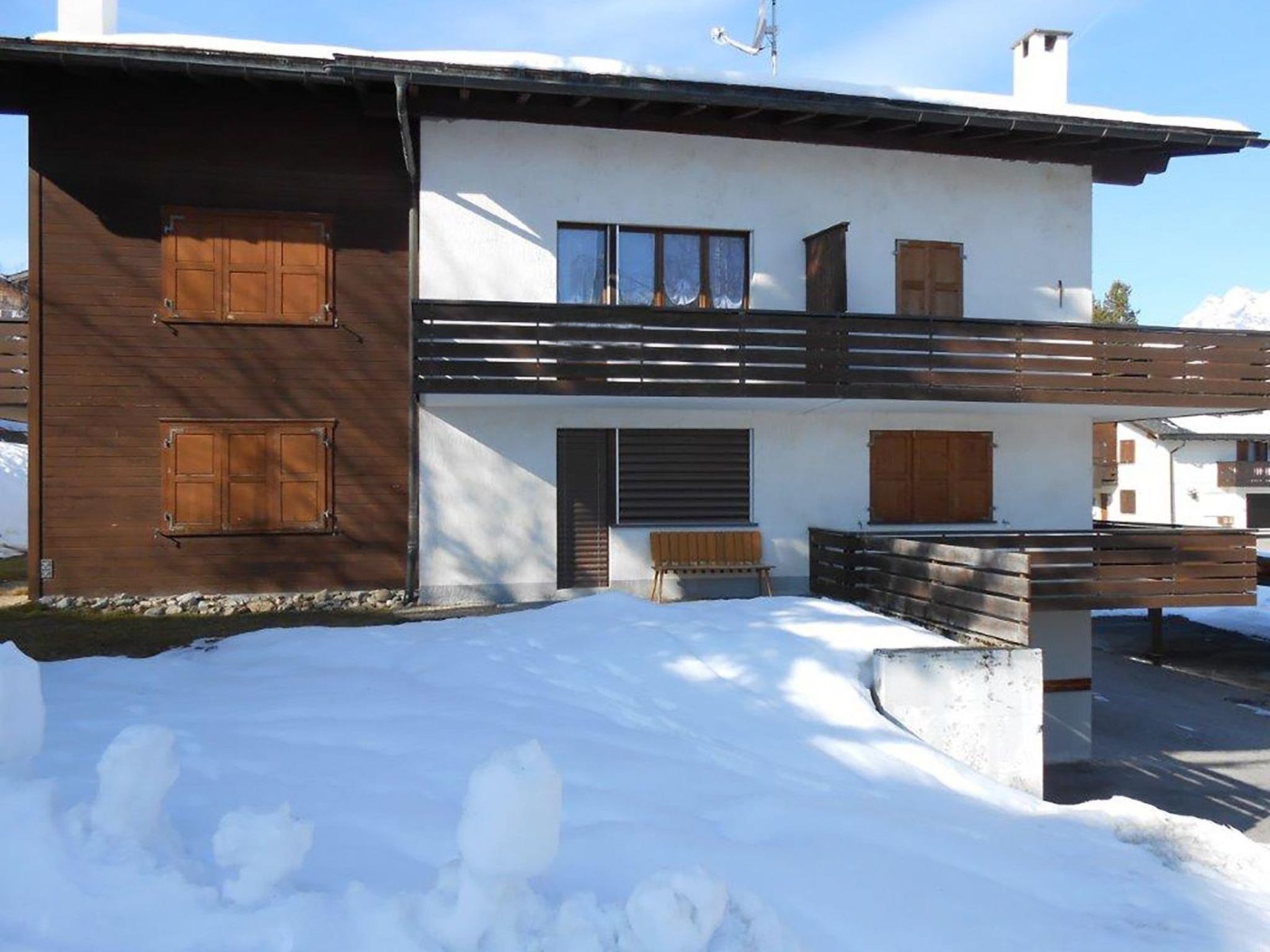 A two-story building with wooden shutters, a balcony, and a snow-covered ground.