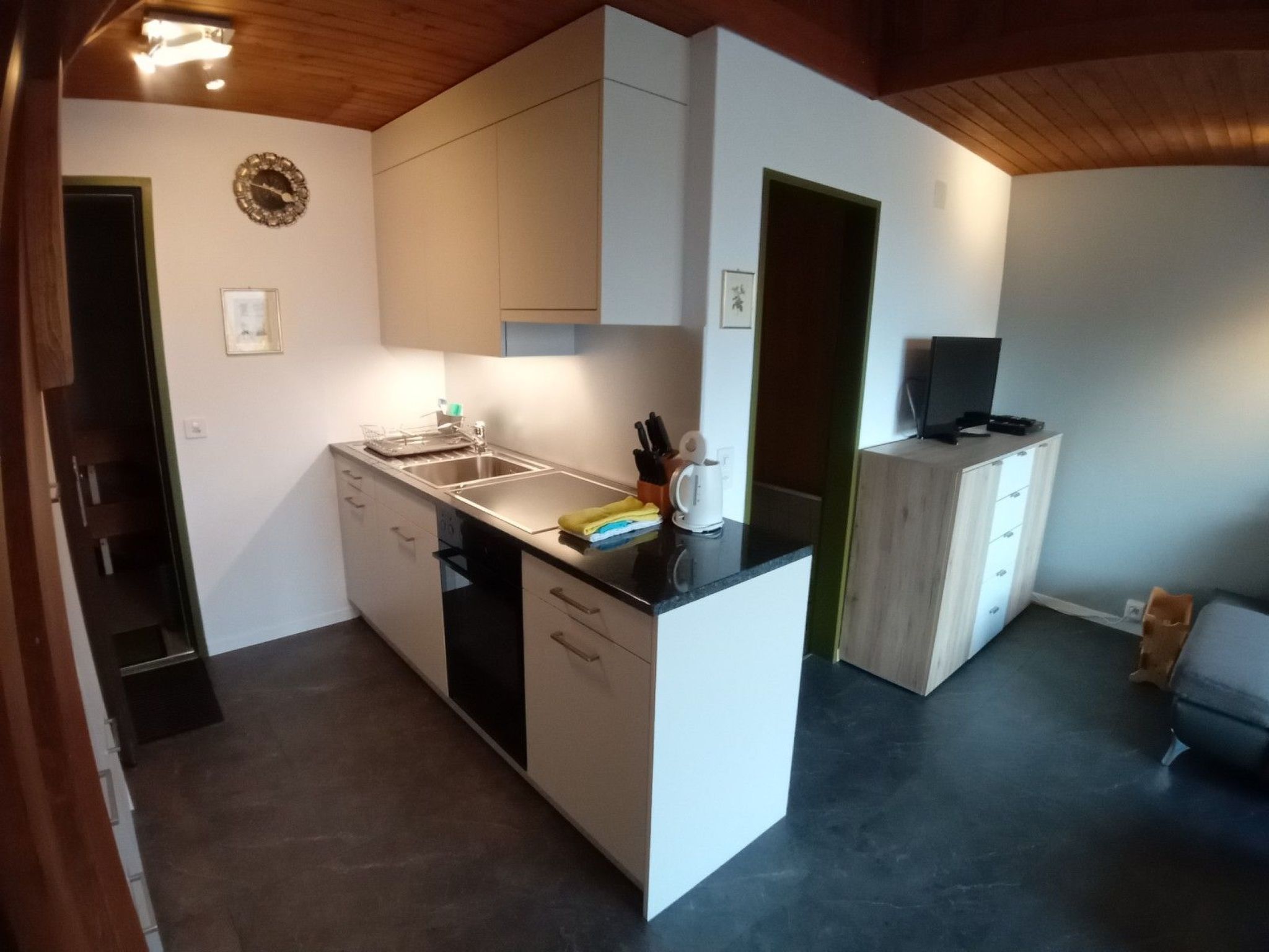 Eine kompakte Küche mit einer zentralen Kochinsel, einem Einbauofen und einer kleinen Sitzecke mit Fernseher.