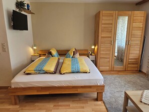 A bedroom with a wooden bed, bedside tables, a wardrobe, and a television mounted on the wall.