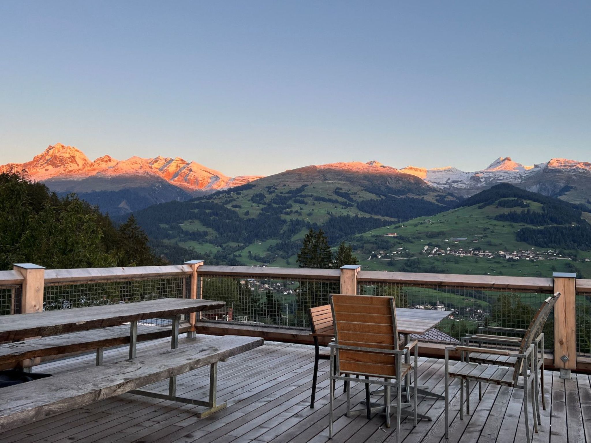 Una terraza de madera con mesas y sillas, con vistas a un paisaje montañoso.