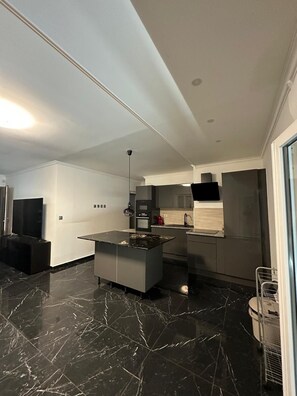 A modern kitchen with a marble countertop island, built-in oven, and a stainless steel refrigerator. - Villa Badia (Empuriabrava)