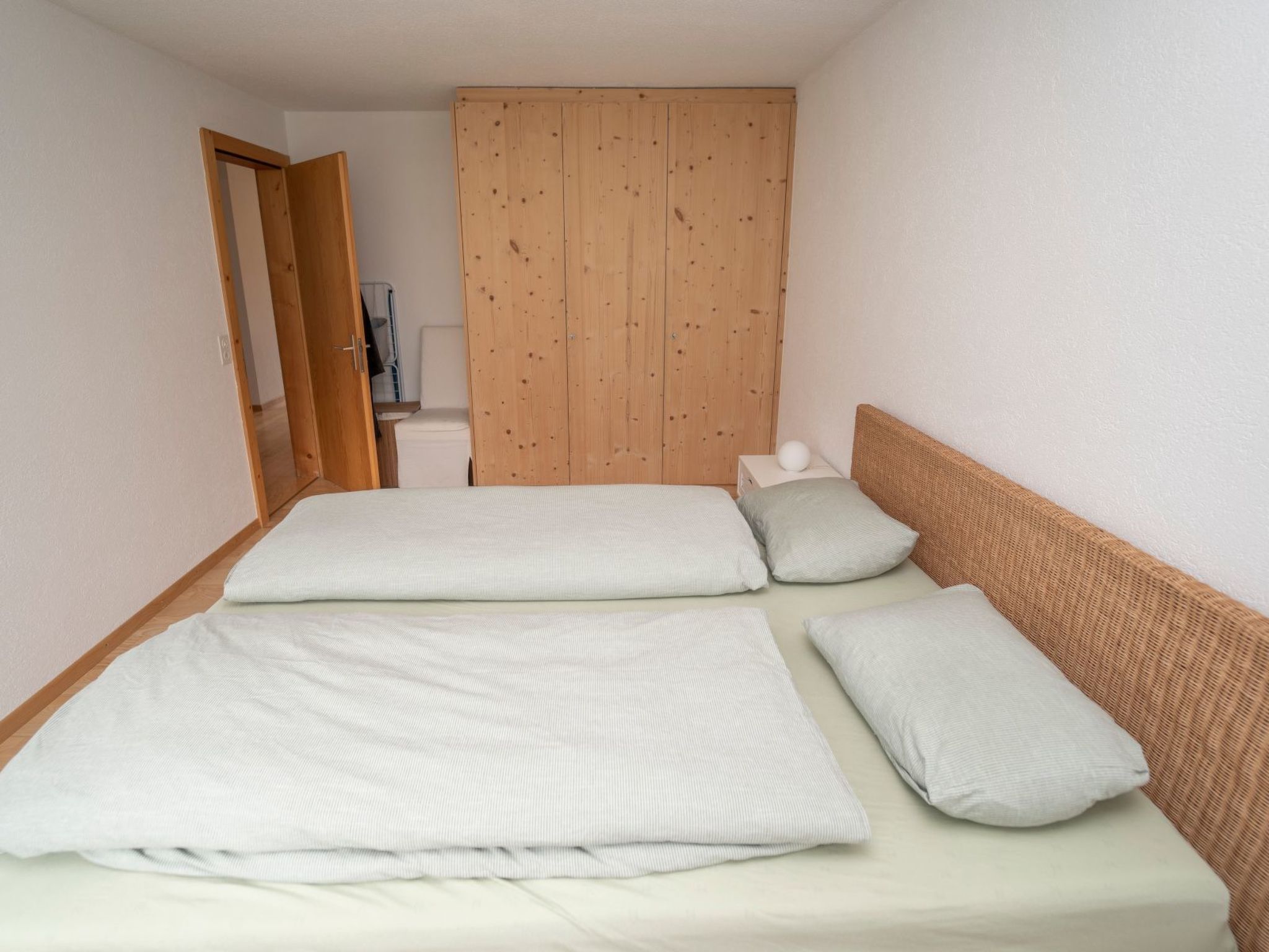 A single-bed room with a wooden wardrobe, a white mattress, and a woven headboard.