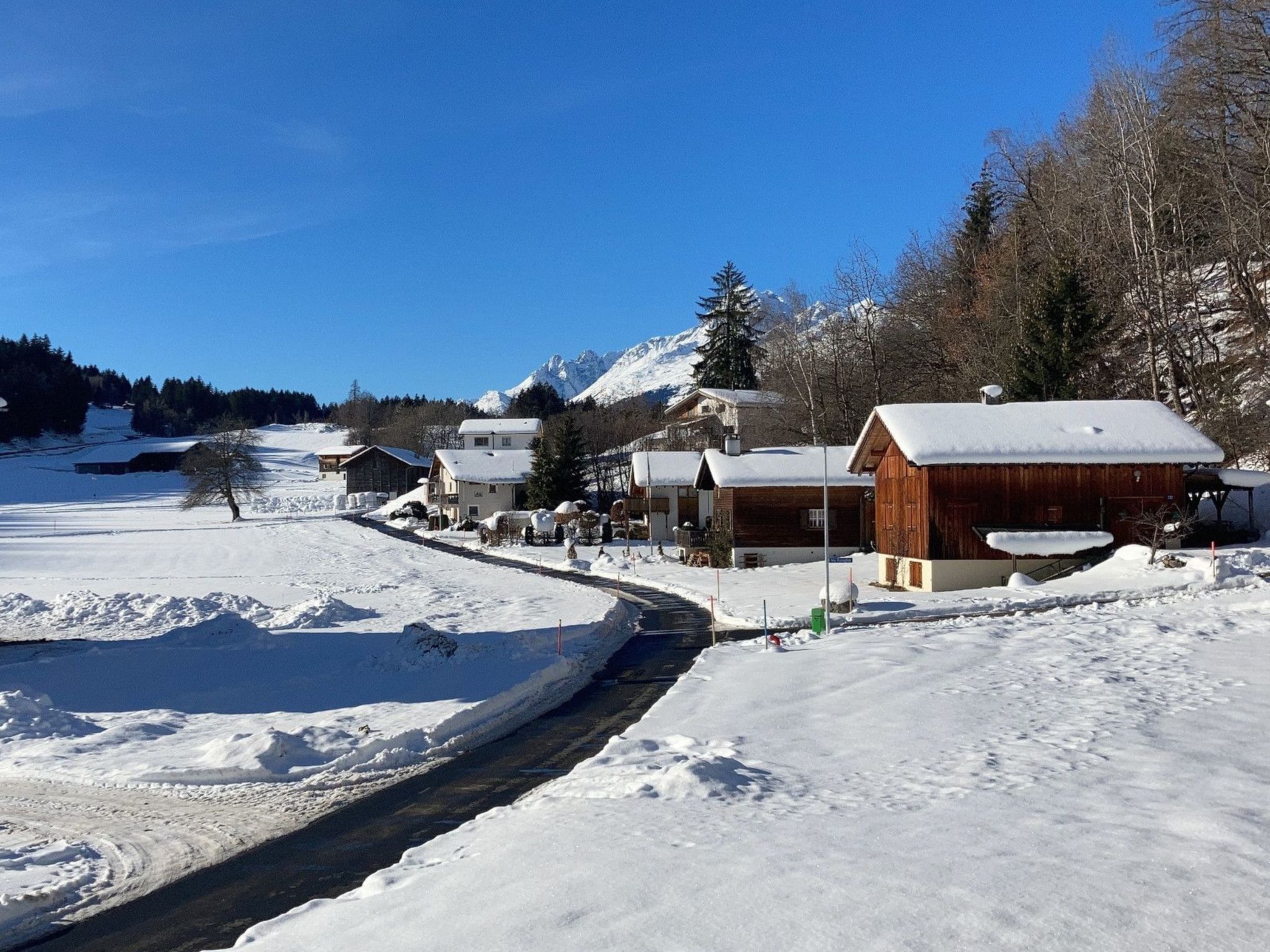 Ein verschneites Dorf mit Holzhäusern, einem klaren Himmel und einem Berg im Hintergrund.