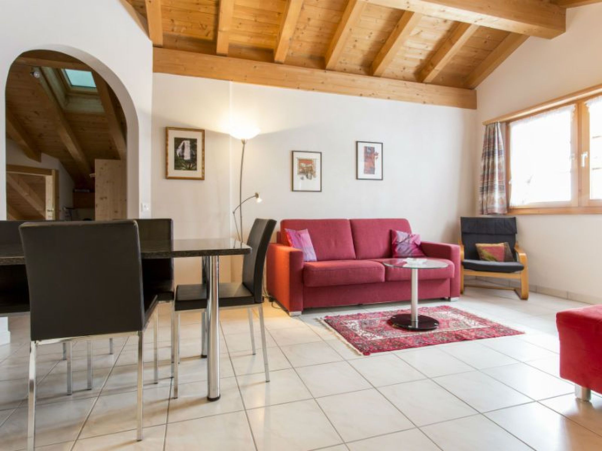 Ein modernes Wohnzimmer mit einem roten Sofa, einem Glastisch und einem Essbereich mit einem schwarzen Tisch und Stühlen.