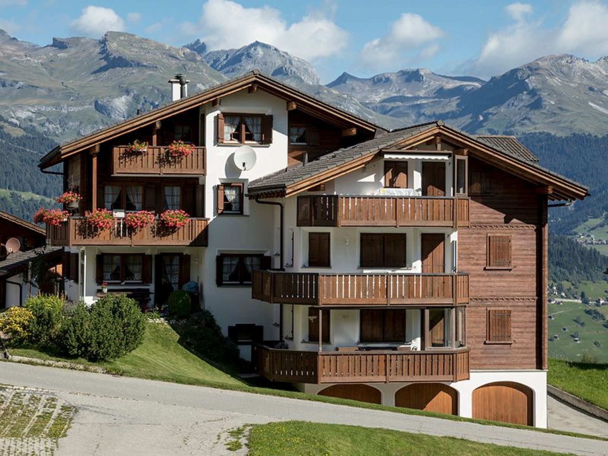 A multi-story chalet with balconies, set against a mountainous backdrop.