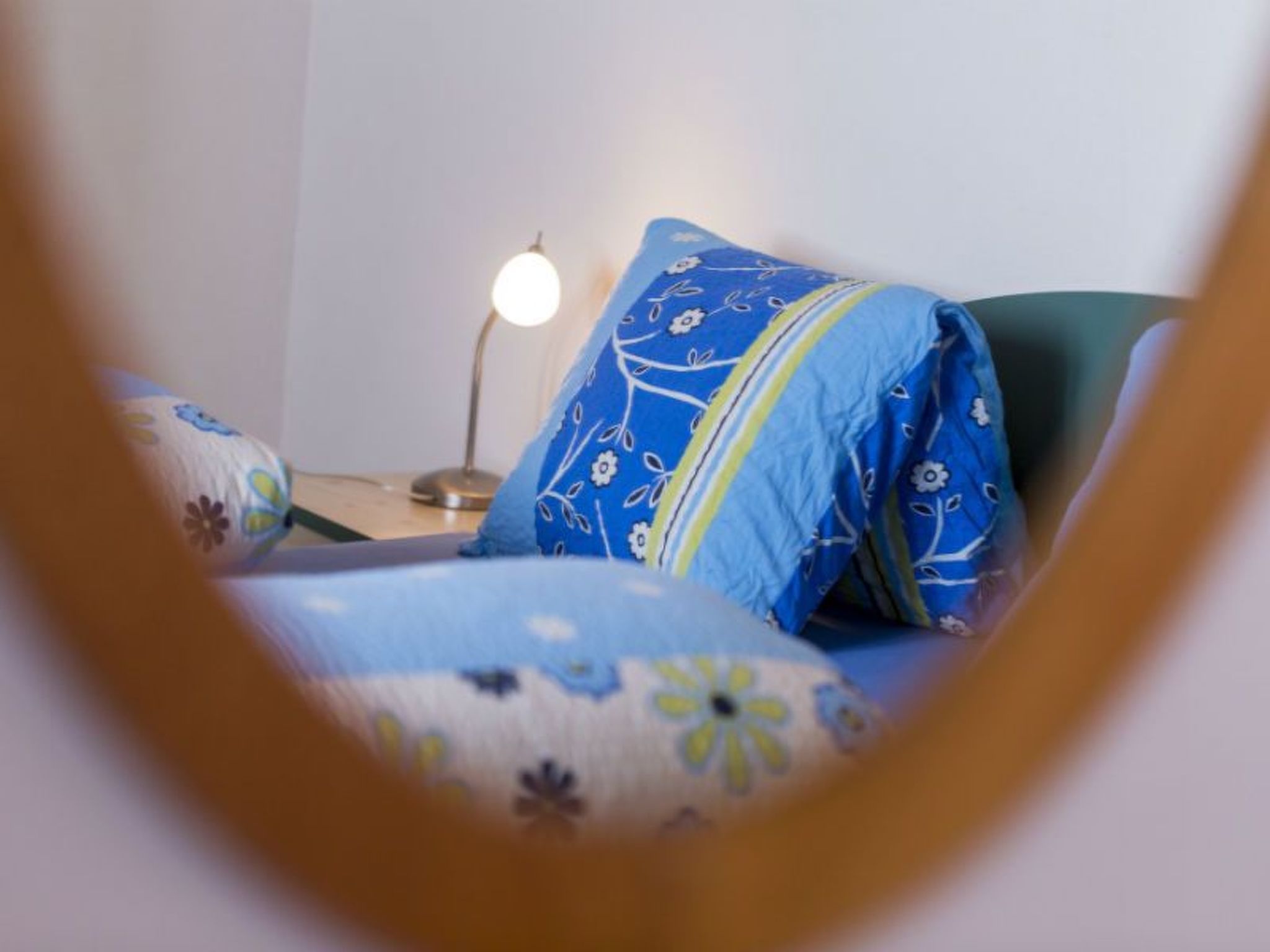 Un dormitorio con una cama cubierta con ropa de cama azul estampada, una lámpara de noche y una mesita de noche con lámpara.