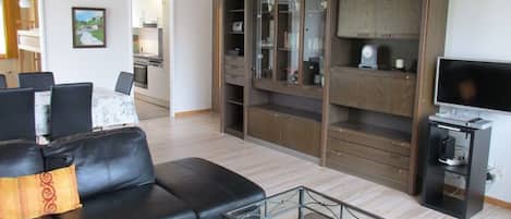 A living room with a black leather sofa, a glass coffee table, a television, and a wooden cabinet with glass doors.