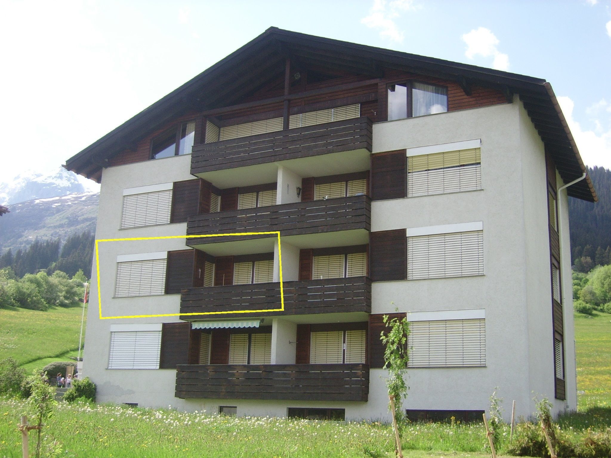 Un edificio de varios pisos con balcones, rodeado de un paisaje verde y montañas al fondo.