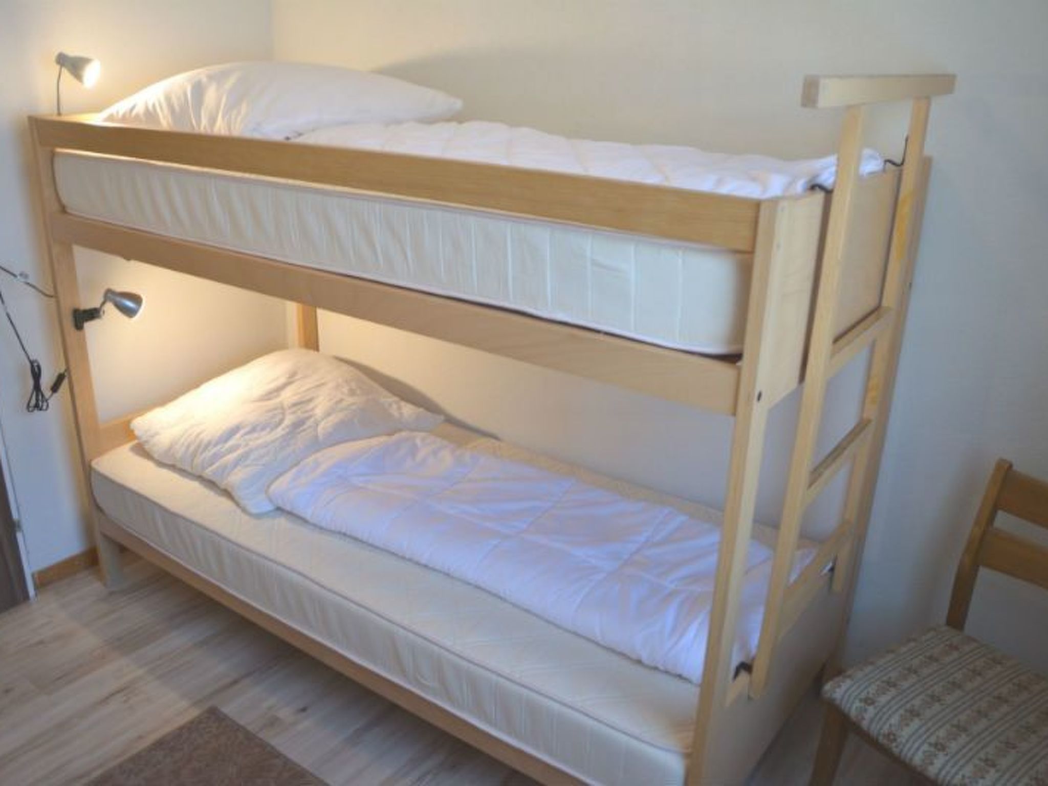 Una cama litera de dos niveles, una escalera de madera y una silla.