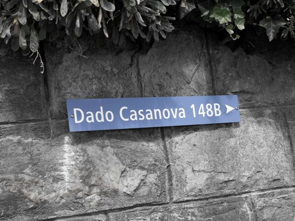 Ein Wegweiser an einer Steinmauer mit dem Text 'Dado Casanova 148B' und einem nach rechts zeigenden Pfeil.