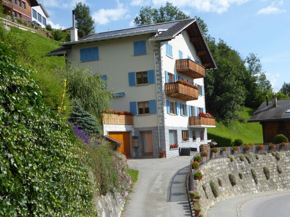 Un edificio de varios pisos con balcones, fachada de piedra y un camino de entrada pavimentado.