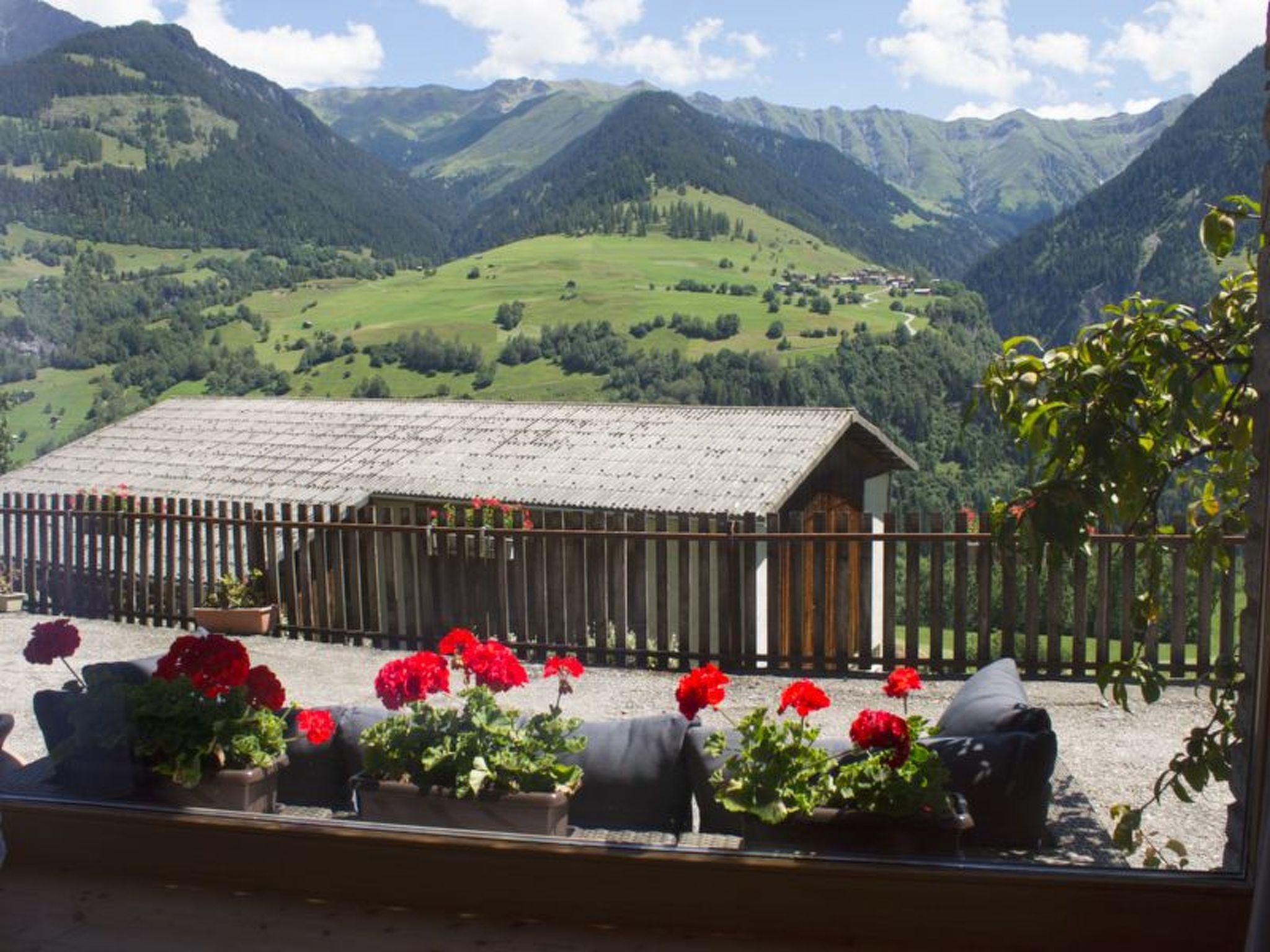 A mountain view with a wooden building and a fenced area with potted plants.