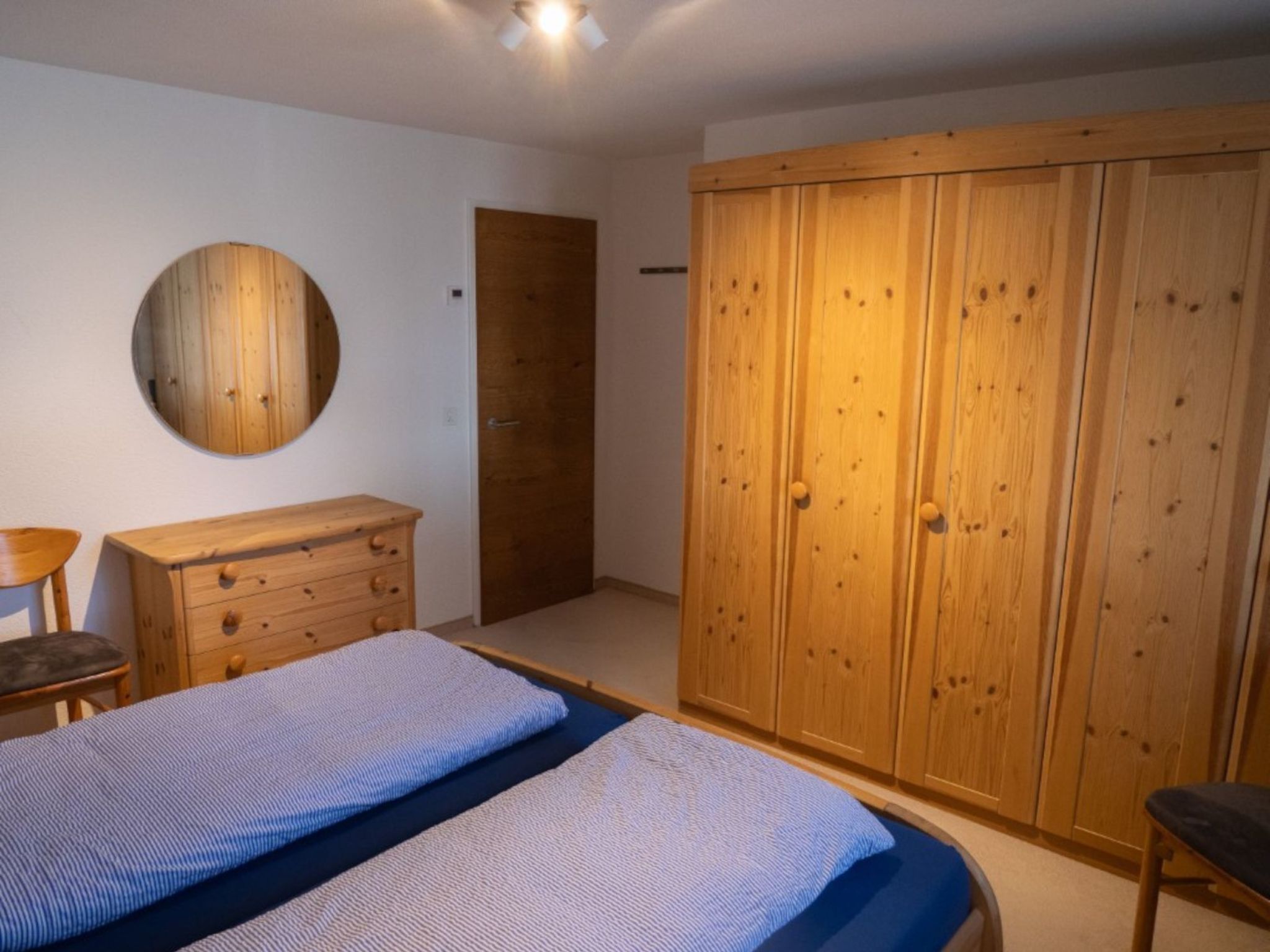 Ein Schlafzimmer mit einem Bett, einem Schminktisch, einem Kleiderschrank und einem runden Spiegel an der Wand.