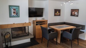 Una sala de estar moderna con chimenea, televisor montado en la pared, una mesa de comedor con sillas y obras de arte en las paredes.