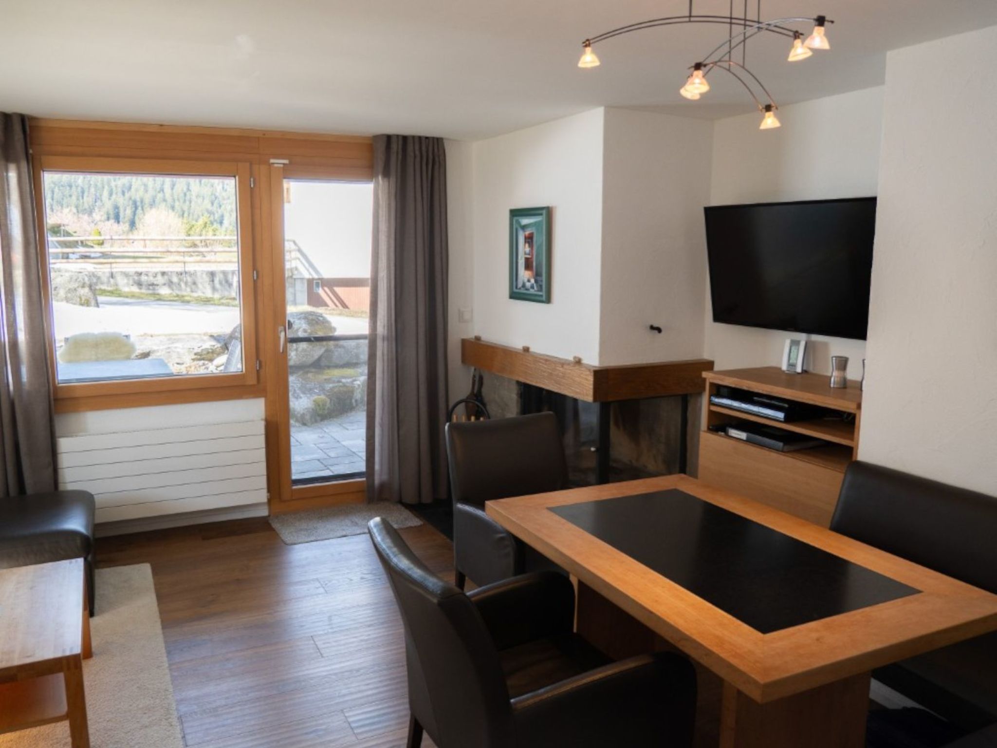 A modern living room with a wooden dining table, black chairs, a flat-screen TV, and a fireplace.
