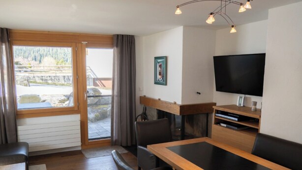 Una habitación con una mesa de comedor, sillas, un televisor y vistas a través de un ventanal corredero.