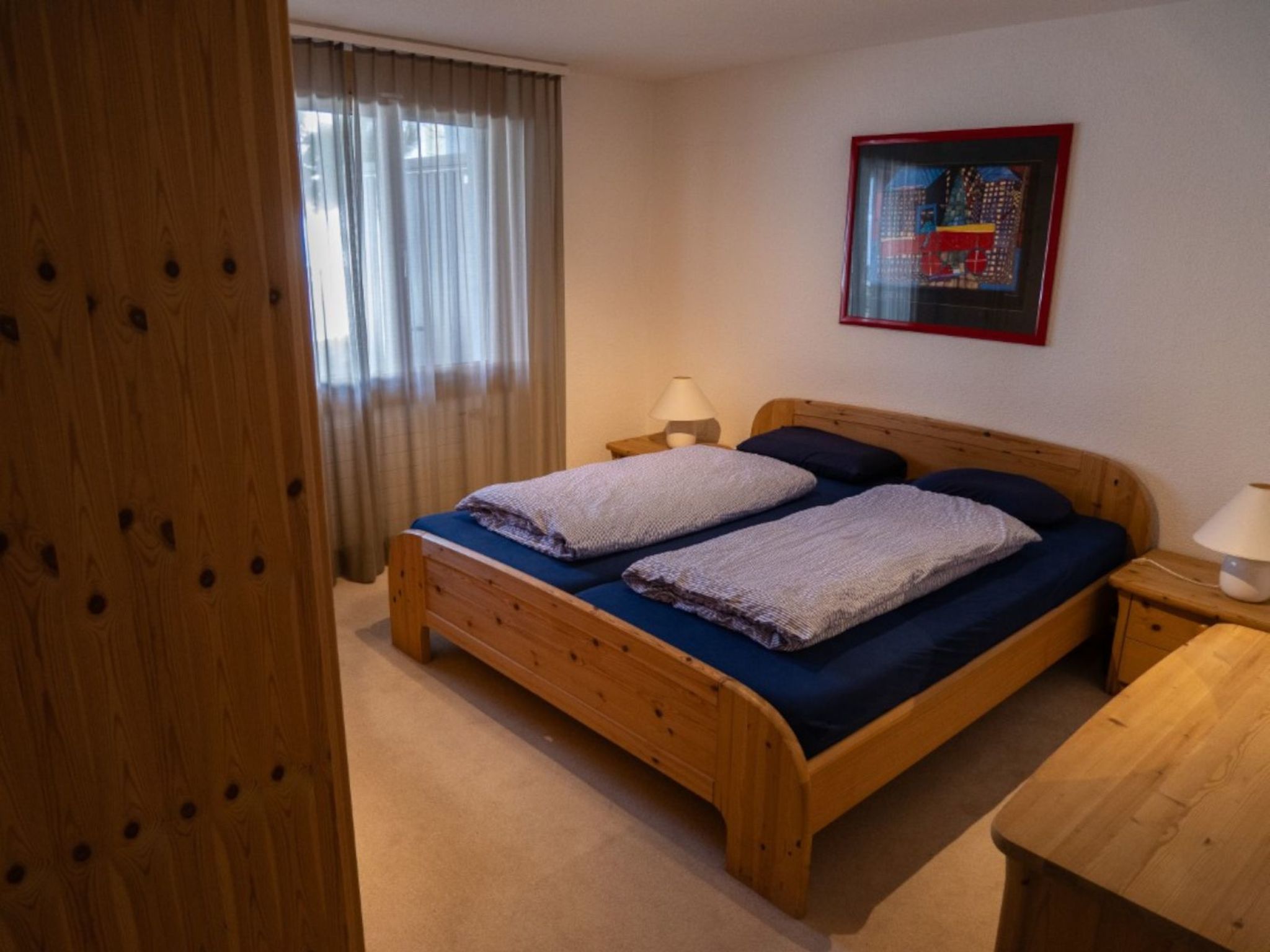 Ein Schlafzimmer mit einem hölzernen Bett, zwei Nachttischen, einem Fenster mit Vorhängen und einem gerahmten Bild an der Wand.