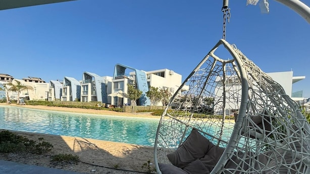 A hanging chair by a poolside with modern buildings in the background. - Fouka North Coast CL3-TW3X-A-G (Marsa Matrouh)