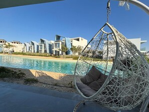 En hængekøjsstol ved en pool med moderne bygninger i baggrunden.