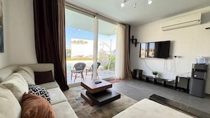 A modern living room with a sofa, a coffee table, a TV, and a sliding glass door leading to an outdoor area. - Fouka North Coast CL3-TW3X-A-G (Marsa Matrouh)