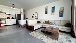 A modern living room with a sectional sofa, a coffee table, and a dining area with a white table and chairs. - Fouka North Coast CL3-TW3X-A-G (Marsa Matrouh)