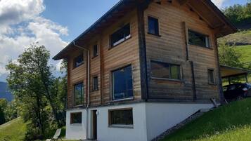 Ein modernes, zweistöckiges Haus mit geneigtem Dach, großen Fenstern und weißer Fassade.