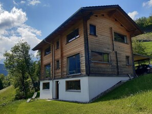 Ein modernes, zweistöckiges Haus mit geneigtem Dach, großen Fenstern und weißer Fassade.