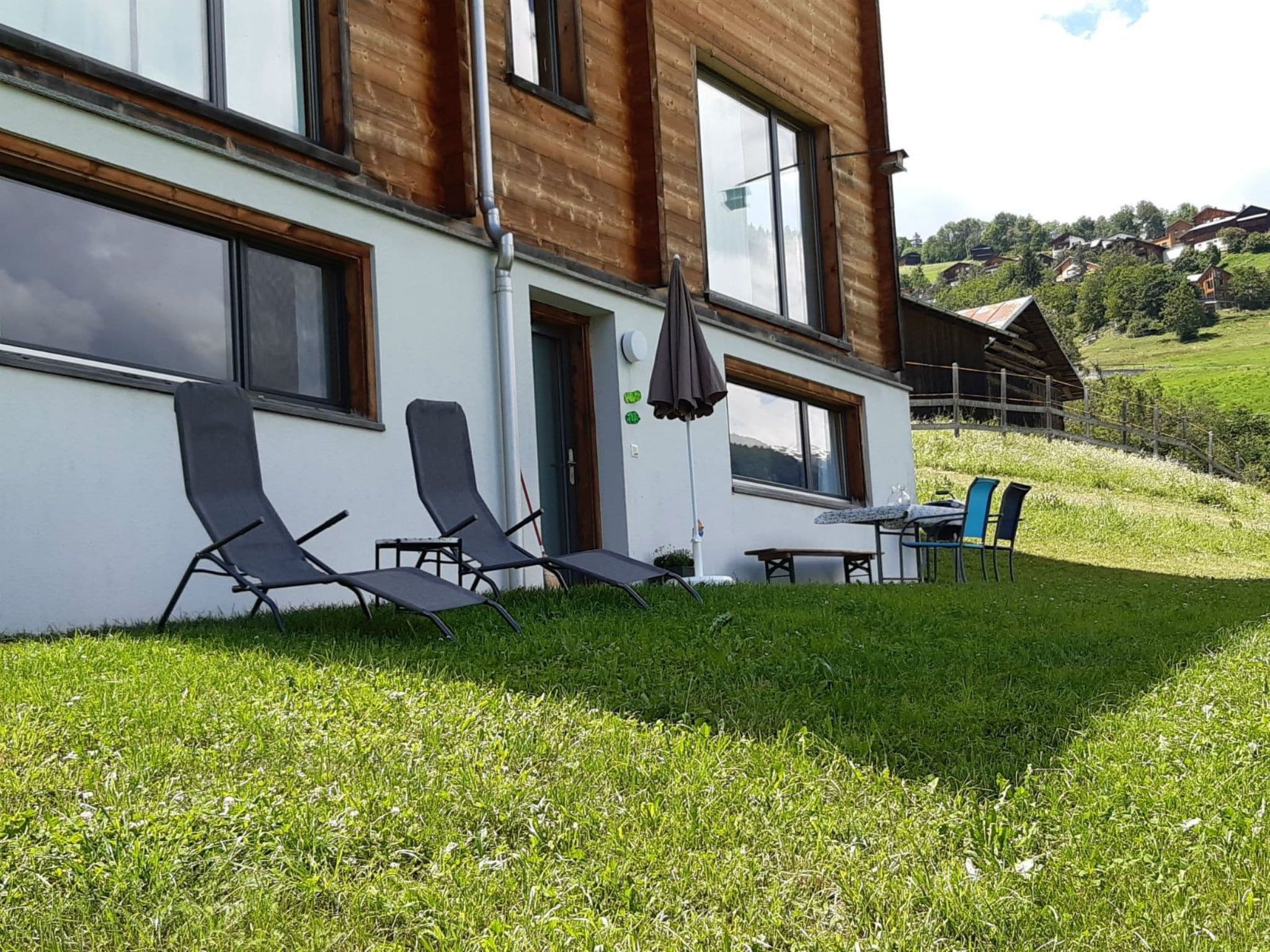 Un bâtiment moderne doté d’un toit plat, de grandes fenêtres et d’une pelouse verdoyante agrémentée de mobilier d’extérieur.