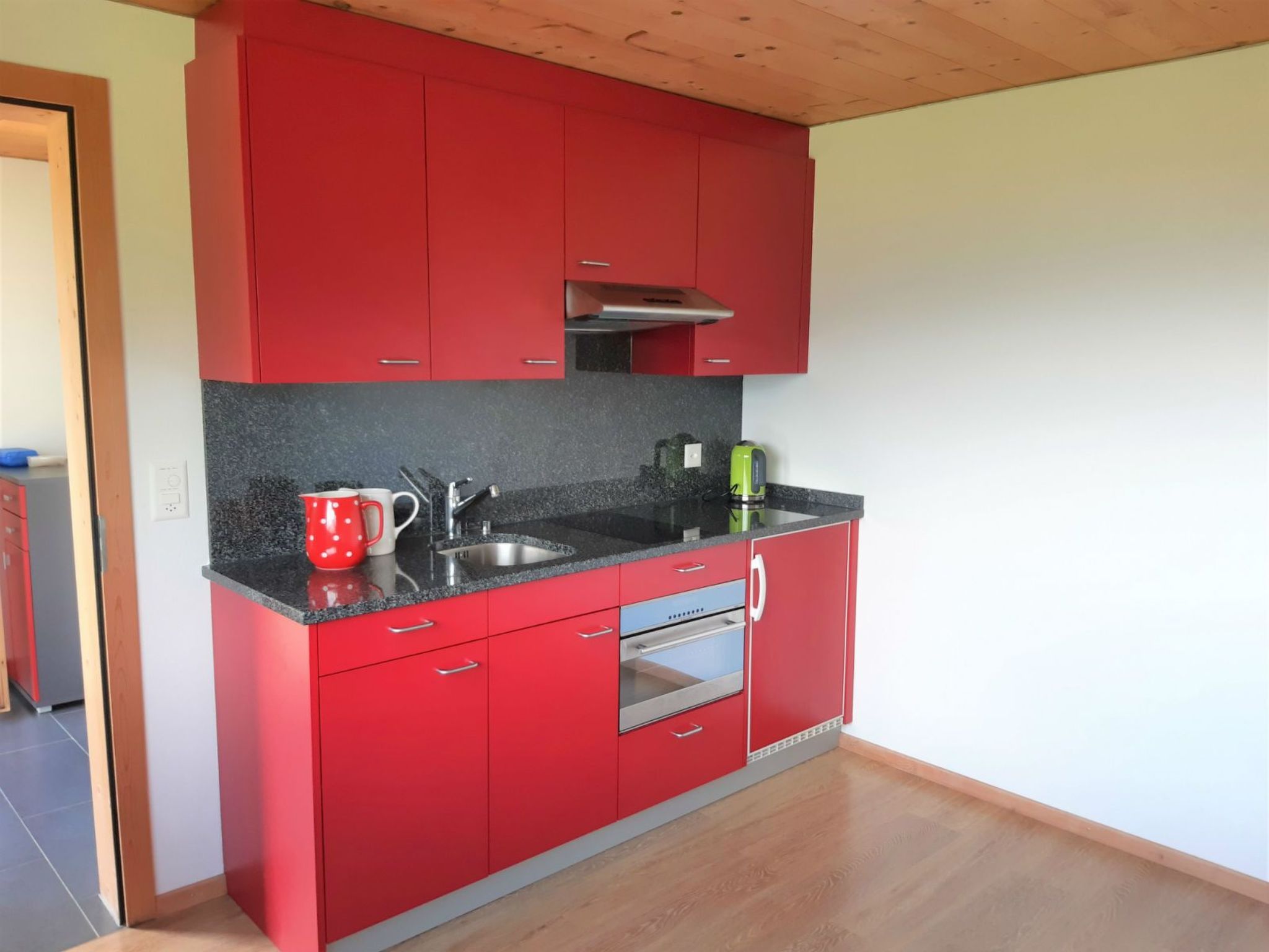 Eine Küche mit roten Schränken, einer Edelstahl-Spüle und einem eingebauten Backofen.