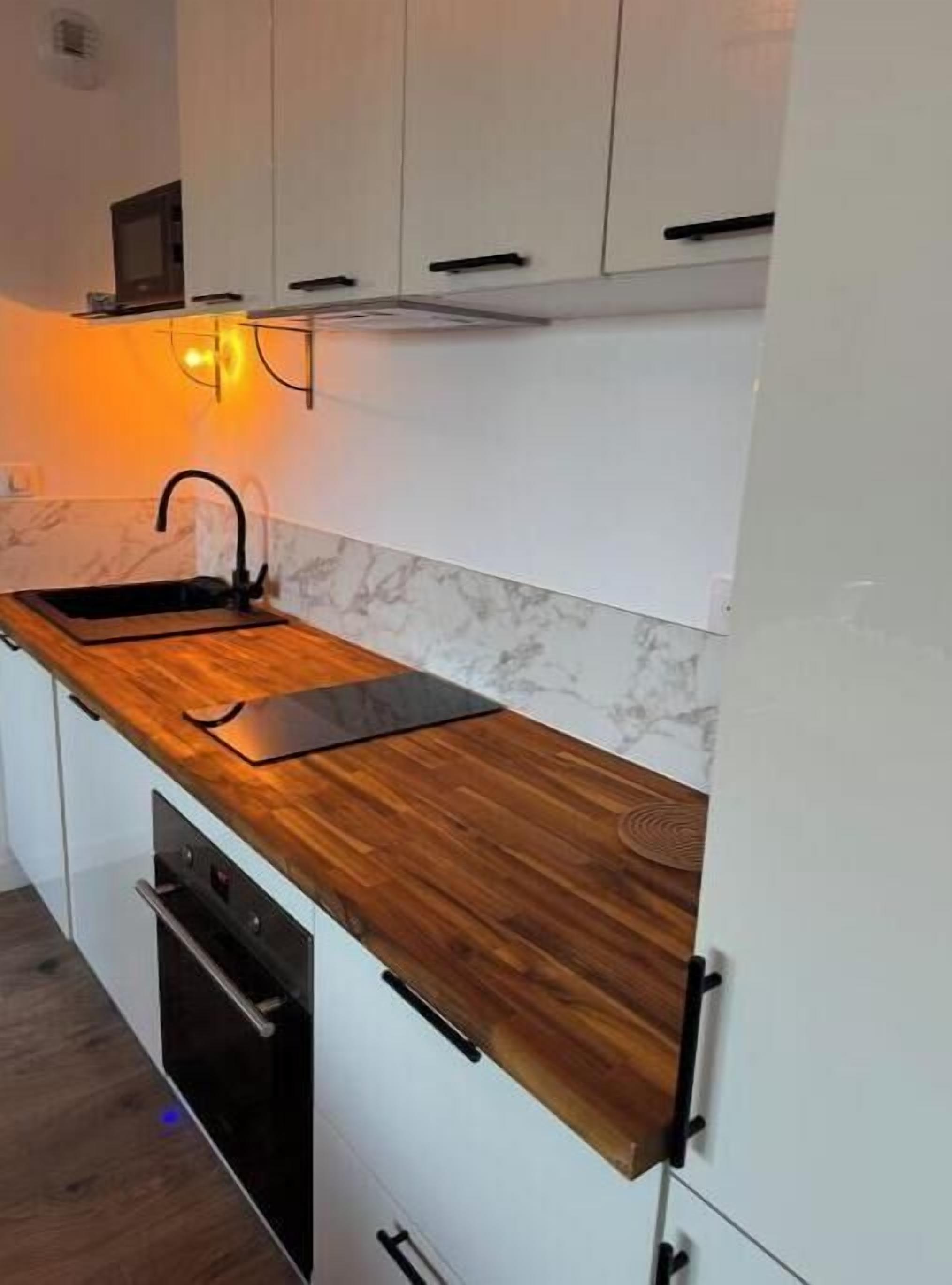 Cucina con piano di lavoro in legno, mobili bianchi, rubinetto nero e forno a incasso.