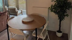 A dining area with a round table, two chairs, a potted plant, and a wall-mounted abstract art piece. - Elegance & Terrace in the heart of the 5 Cantons - Beaches on foot (Anglet)