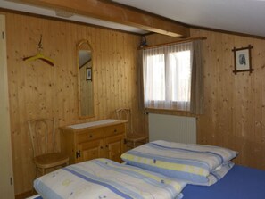Habitació amb panells de fusta, dos llits, un taulell, una cadira, una finestra amb cortines i un mirall.