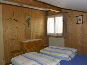 Ein Zimmer mit Holzwandverkleidung, ausgestattet mit einem Bett, einem Sessel, einem Schminktisch und einem Fenster mit Vorhängen.