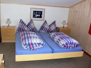 Cama doble con ropa de cama azul, dos mesitas de noche con lámparas, un cuadro enmarcado en la pared y un panel de pared de madera.