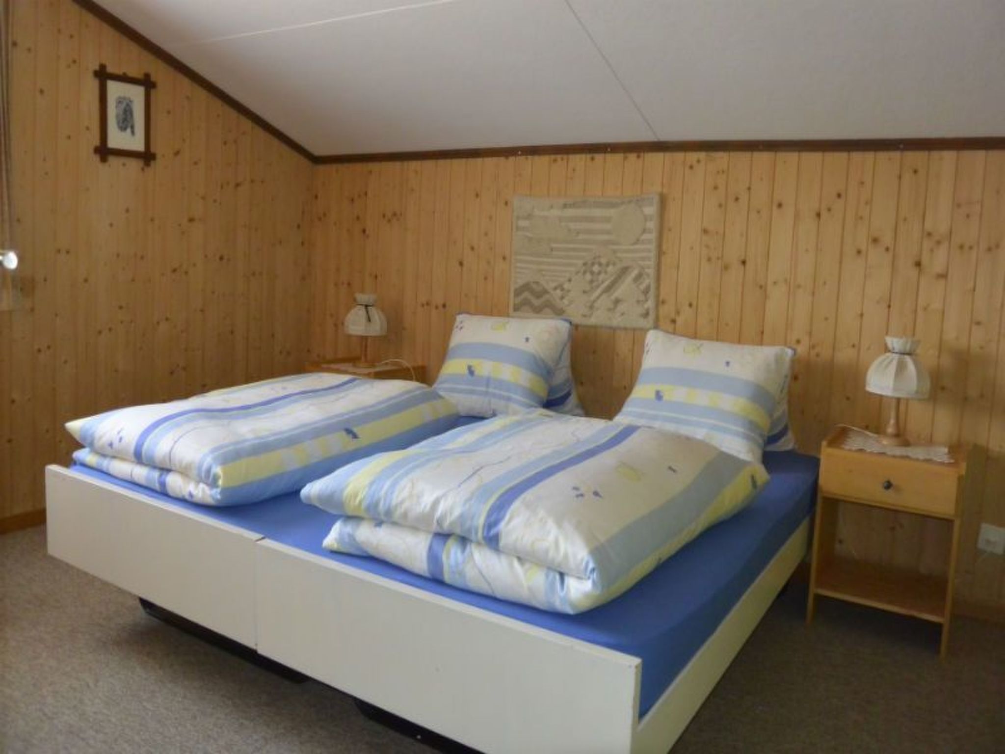 A double bed with striped bedding in a room with wooden walls and a sloped ceiling.