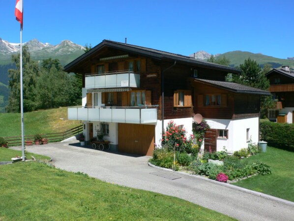 Ein zweigeschossiges Chalet mit Balkon, Flagge und Bergblick.