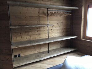 Een kamer met houten wanden, een raam en ingebouwde planken met haken.