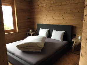 Een houten kamer met een bed, een raam en een nachtkastje.