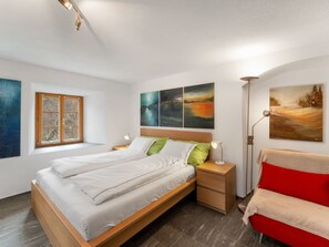 A modern bedroom with a wooden bed, a nightstand, a floor lamp, and artwork on the walls. - Pacifica und Romantica in Cumpadials, (Cumpadials), 76002B by Interhome (Cumpadials)