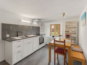 A modern kitchen with white cabinetry, a grey backsplash, and a dining area with a wooden table and chairs. - Pacifica und Romantica in Cumpadials, (Cumpadials), 76002B by Interhome (Cumpadials)