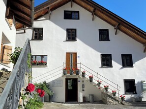 A white building with a wooden roof, multiple windows, and a staircase leading to the entrance.