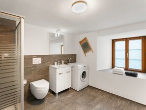 A modern bathroom with a toilet, sink, and washing machine. - Pacifica und Romantica in Cumpadials, (Cumpadials), 76002B by Interhome (Cumpadials)