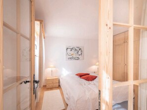 A bedroom with a bed, a nightstand, a lamp, a wooden wardrobe, and a wall with a piece of abstract art.