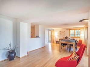A spacious living area with a dining table and chairs, a red sofa, and a potted plant.